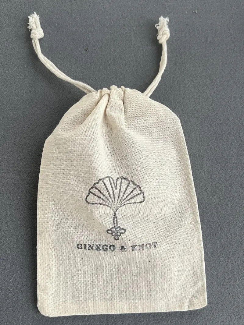 A natural cotton drawstring pouch stamped with the Ginkgo & Knot logo.