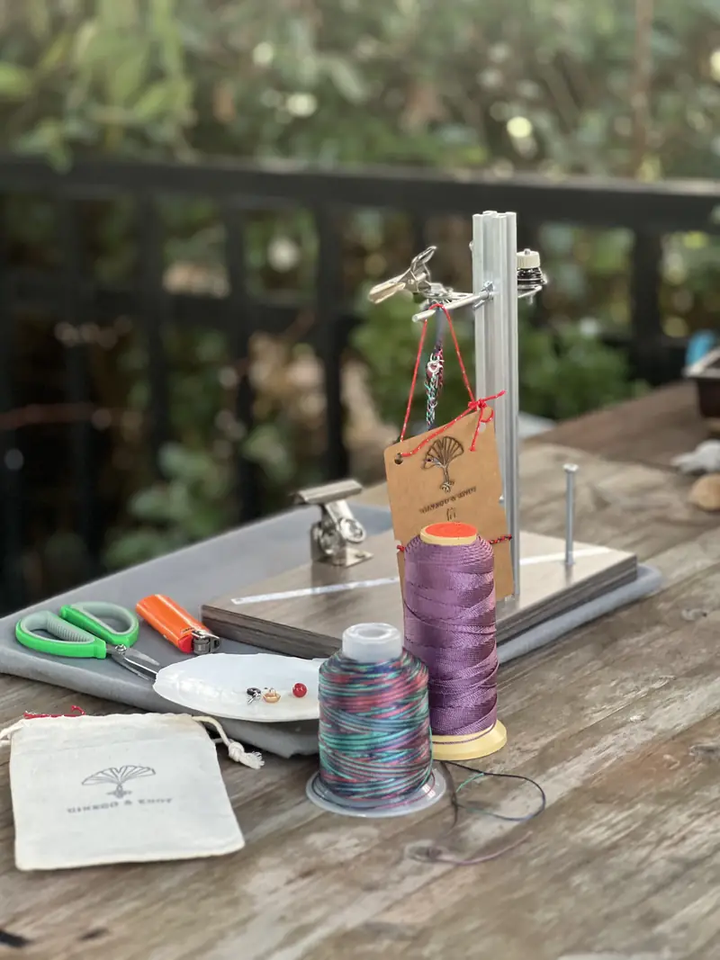 The backyard workbench: a knotting stand holding a blessing card, spools of purple and rainbow cord, scissors and a stamped cotton pouch.